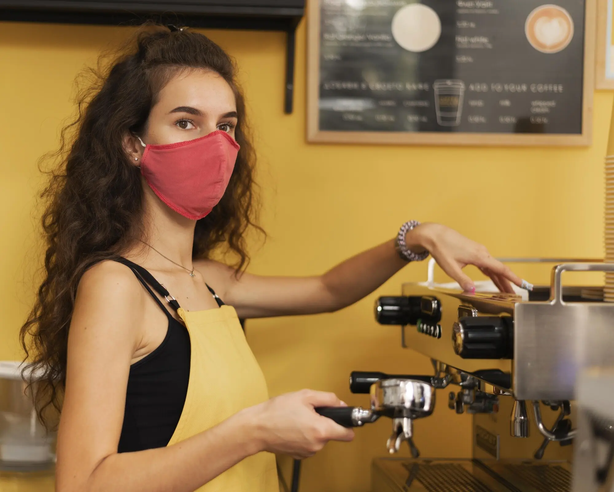 Barista mit medizinischer Maske beim Zubereiten von Kaffee in Innenräumen.