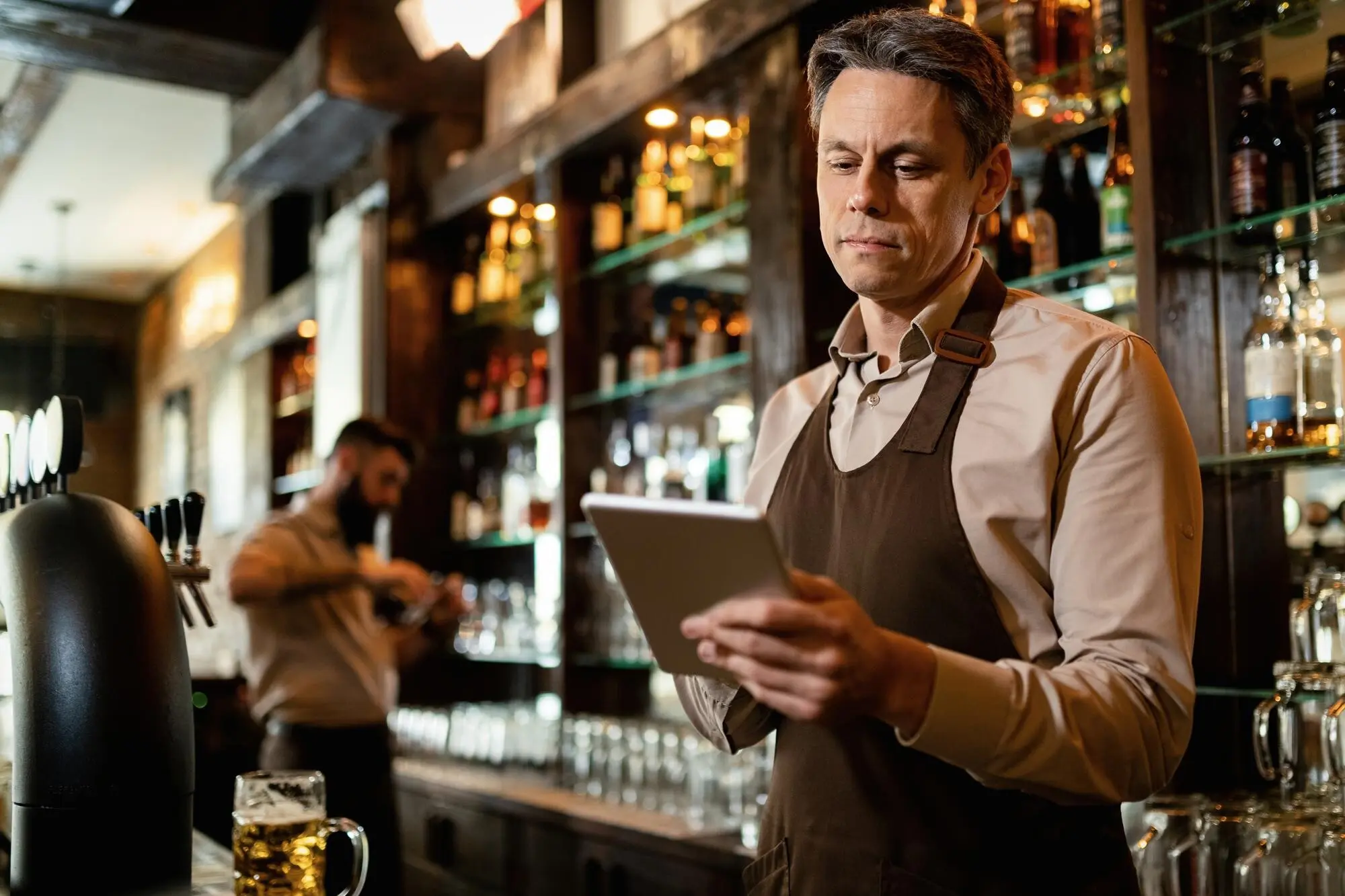 Lächelnder Kellner mittleren Alters, der bei der Arbeit in einer Bar ein Touchpad benutzt, praxisnah und nachvollziehbar.