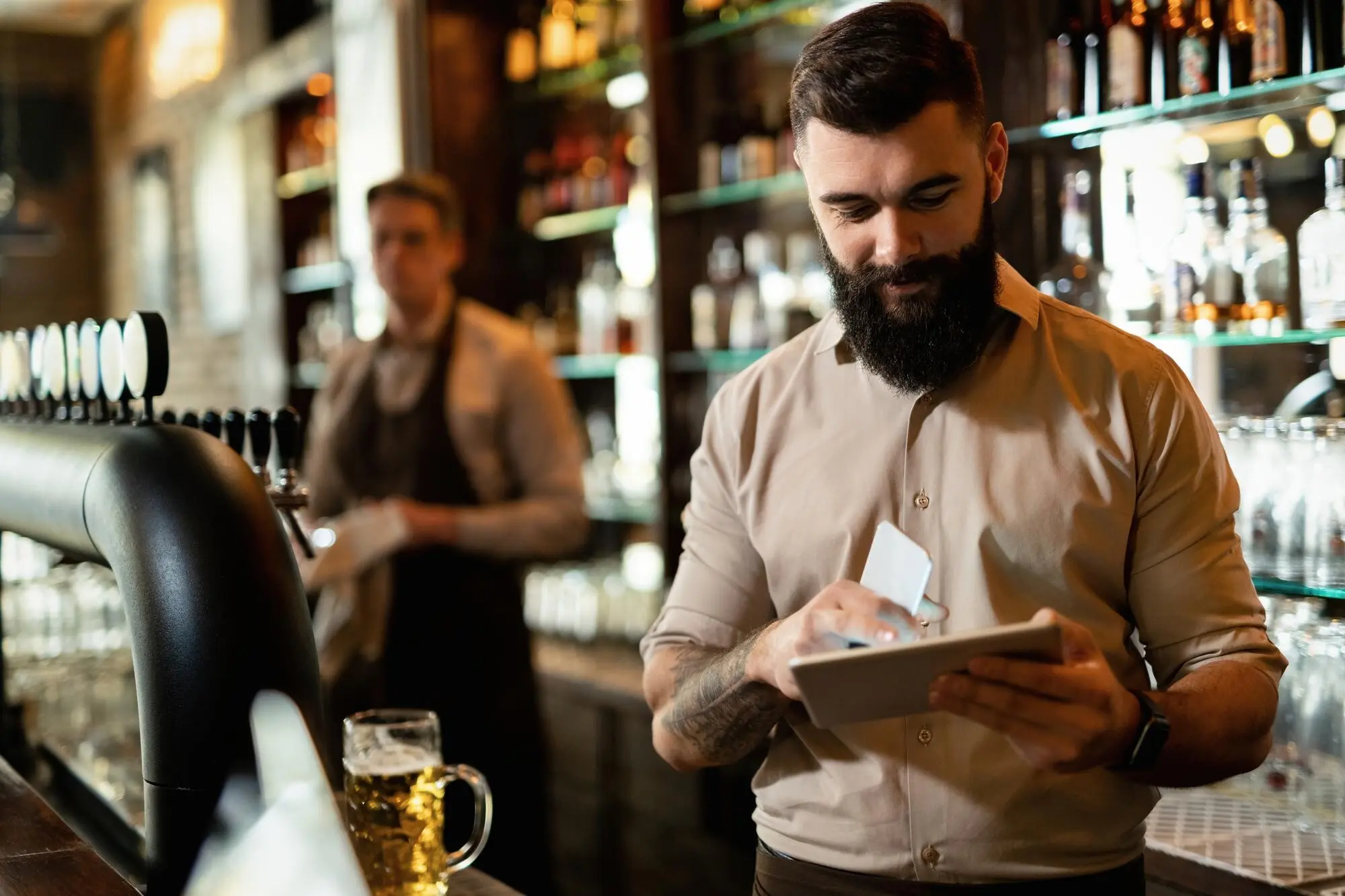 Ein junger, glücklicher Barista arbeitet in einer Bar und surft auf einem Touchpad im Internet, praxisnah und nachvollziehbar.